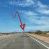 A red arrow points to a distant car on a straight, empty desert highway under a blue sky with scattered clouds.