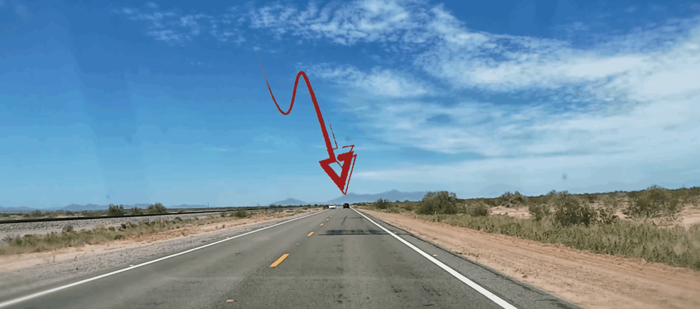 A red arrow points to a distant car on a straight, empty desert highway under a blue sky with scattered clouds.
