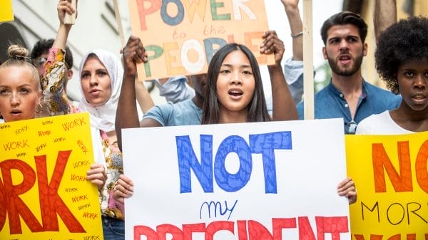 A diverse group of protesters hold signs, including one reading "NOT my PRESIDENT," while expressing their opinions at a rally.