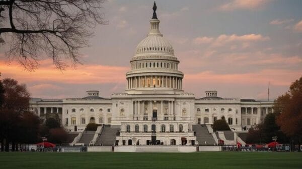 The United States Capitol building at sunset, with a pink-orange sky and trees framing the foreground.