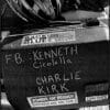 A motorcycle case with stickers and handwritten names: "F.B.: Kenneth Cicolella" and "Charlie Kirk." Stickers include "BACK THE BLUE" and "ZOMBIES EAT BRAINS!!! REPUBLICANS ARE SAFE.
