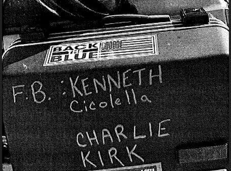 A motorcycle case with stickers and handwritten names: "F.B.: Kenneth Cicolella" and "Charlie Kirk." Stickers include "BACK THE BLUE" and "ZOMBIES EAT BRAINS!!! REPUBLICANS ARE SAFE.
