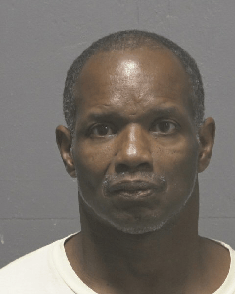 A middle-aged man with short hair and a mustache looks directly at the camera against a plain gray background.