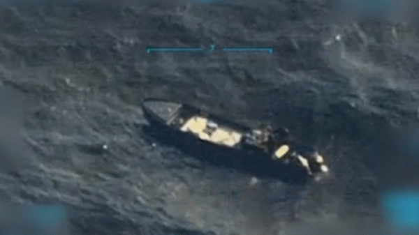 Aerial view of a dark-colored ship sailing in the ocean, seen through a targeting or surveillance camera interface.