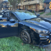 A black car with front-end damage is parked on grass beside a road in a residential area; Cleveland Police logo is in the top right corner.