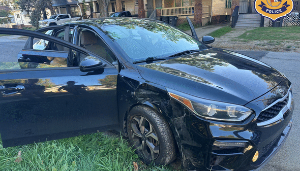 A black car with front-end damage is parked on grass beside a road in a residential area; Cleveland Police logo is in the top right corner.