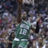 A basketball player in a green Boston jersey, number 12, jumps for a layup near the hoop during a game against Washington.