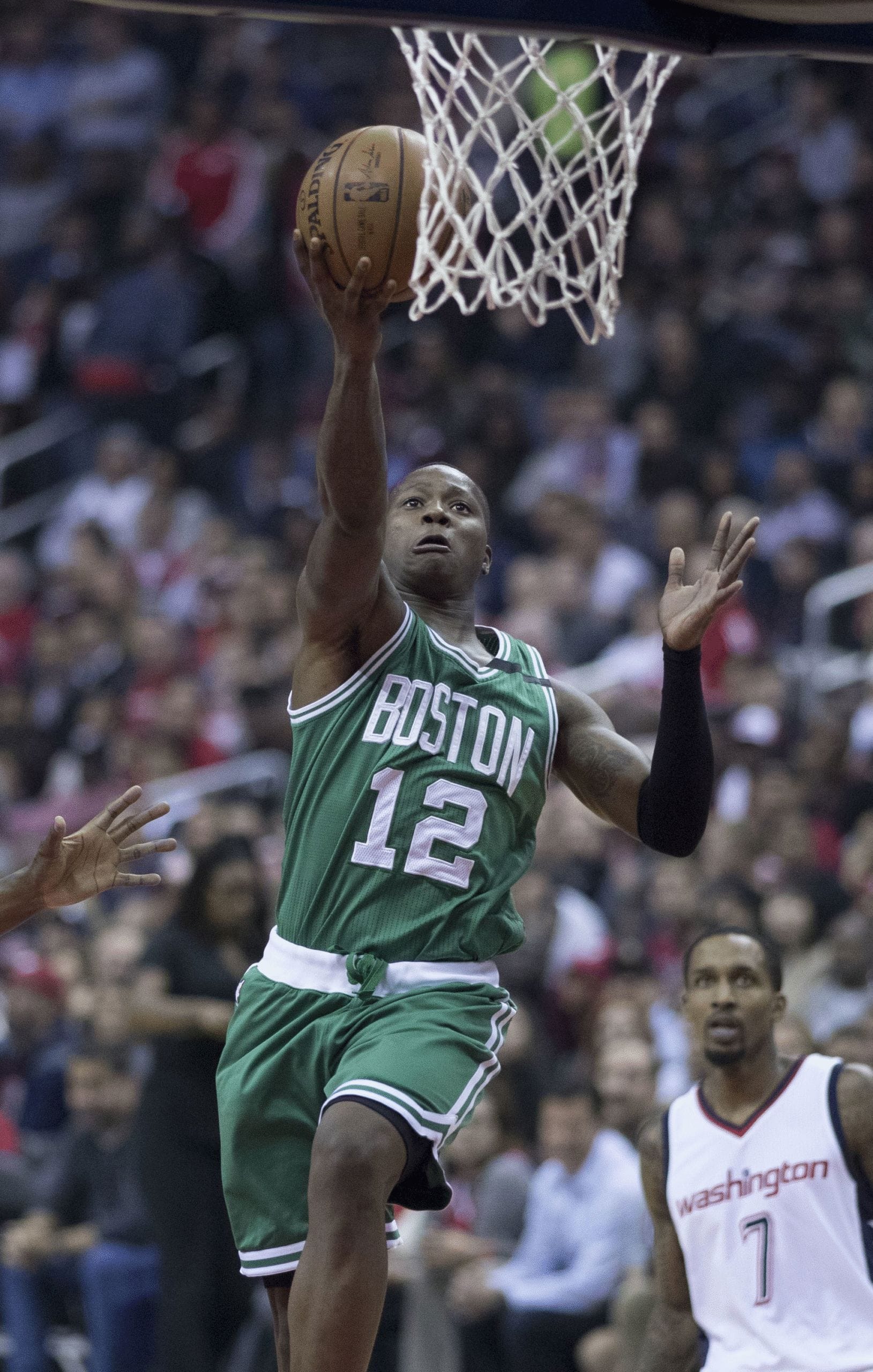 A basketball player in a green Boston jersey, number 12, jumps for a layup near the hoop during a game against Washington.