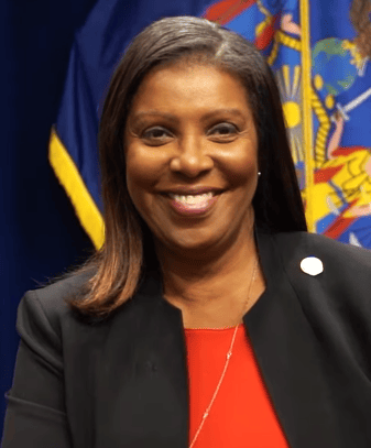 A woman in a black blazer and red top smiles in front of a blue and yellow flag with a colorful crest.