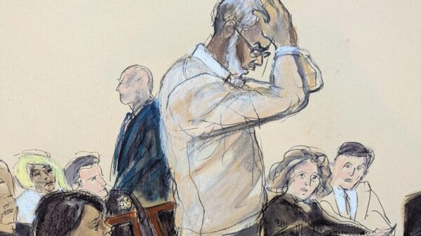 A courtroom sketch shows a man standing, holding his head in distress, while others sit and watch attentively.