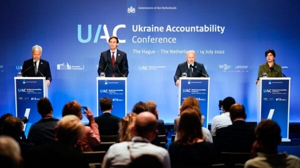 Four speakers stand at podiums on stage at the Ukraine Accountability Conference in The Hague, addressing an audience, with a blue backdrop displaying event details and logos.